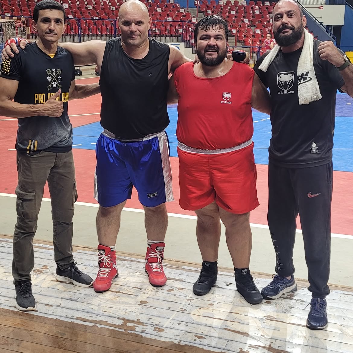 Dois boxeadores e dois membros da equipe com os braços dados, posando na plataforma da arena