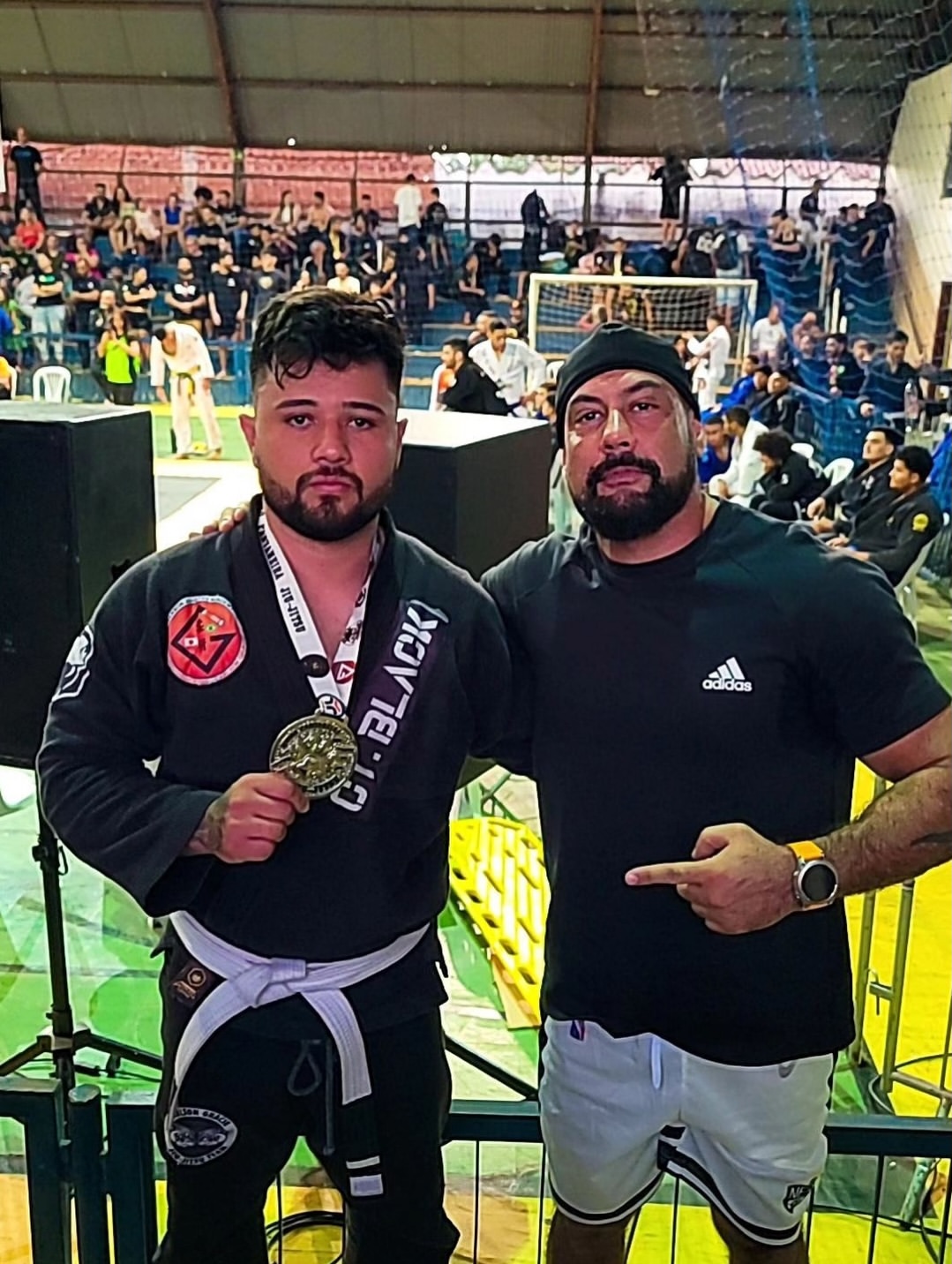 Atleta de kimono e professor posando com medalha no campeonato
