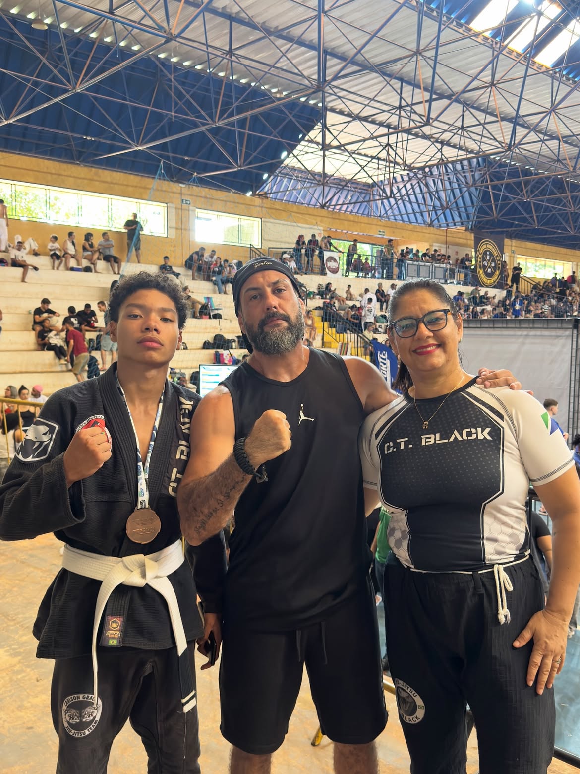 Atleta, professor e companheira posando com medalha de Jiu-Jitsu
