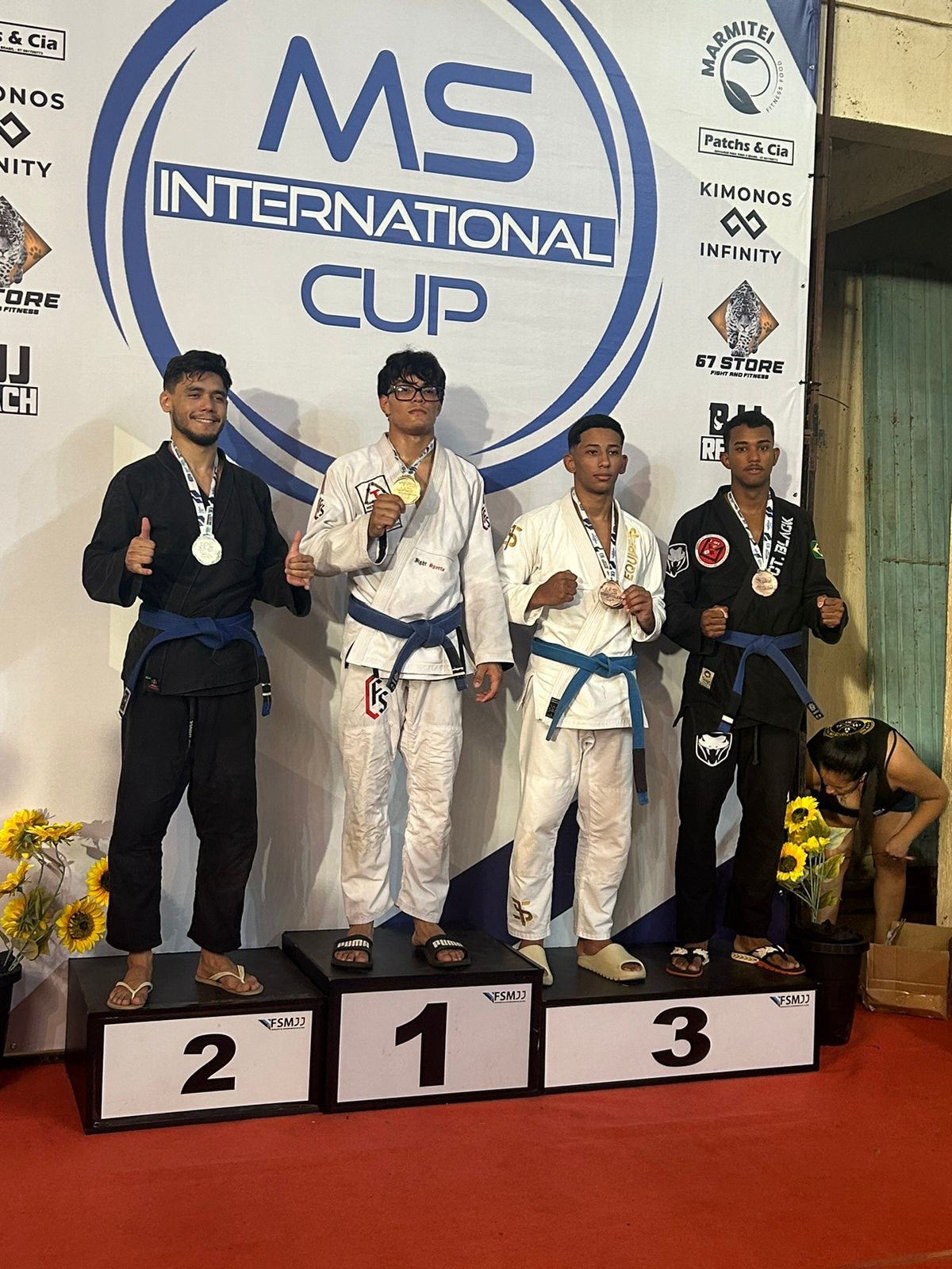 Quatro atletas de Jiu-Jitsu posando no pódio