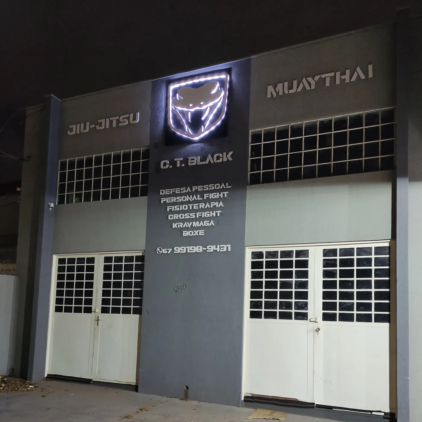 Fachada do CT Black à noite, com o logotipo iluminado e as modalidades na parede